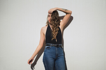 Chica joven delgada con pelo largo ondulado posando delante de pared blanca con luz muy dura