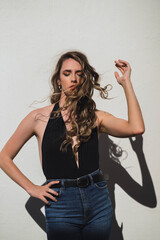 Chica joven delgada con pelo largo ondulado posando delante de pared blanca con luz muy dura