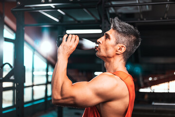 Fototapeta na wymiar Lifestyle portrait of handsome muscular man drinking water in the gym. Middle aged man drinks water in the gym.