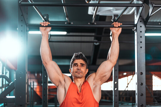 Slim muscular man doing pullups shirtless in the gym, high contrast image.