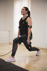 A pretty young girl lifting weights while wearing an electrostimulation vest. - obrazy, fototapety, plakaty