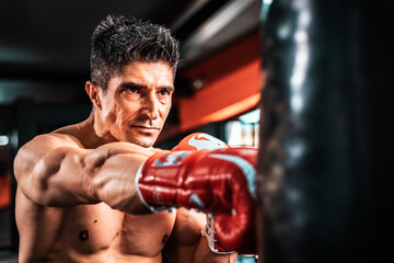 Fototapeta na wymiar Caucasian fighter man wear boxing red gloves and punching forward with one fist to camera in the fitness sport gym. Make looking forward with serious face. Exercise for a healthy body.