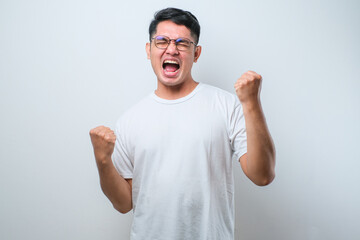 Young asian man wearing casual shirt standing very happy and excited doing winner gesture with arms...