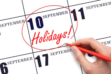 Hand drawing a red circle and writing the text Holidays on the calendar date 10 September . Important date.