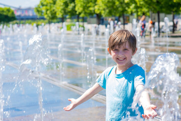 Naklejka premium happy child plays in a dry fountain. joyful smiling boy stands wet in the fountain