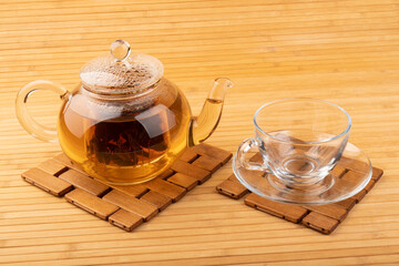 Glass cup of hot aromatic tea and teapot on bamboo mat background.