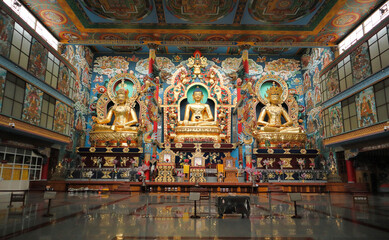 Fototapeta premium A View of the interiors of the Tibetan monastery with mammoth statues of three Buddhas in Gold decoration at Bylakuppe town of Karnataka state in India.