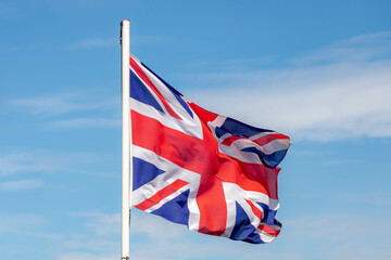 The official national flag of England on the pole waving in the air with blue sky as background,...