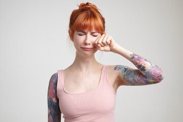 Indoor portrait of young ginger female posing over white wall almost crying