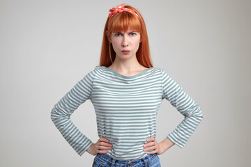 Indoor portrait of young ginger female posing over white wall looking into camera with sad facial...