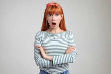 Indoor portrait of young ginger female posing over white wall looking into camera with surprised facial expression