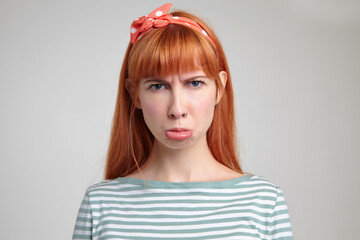 Indoor portrait of young ginger female posing over white wall curving her lip with sad facial...