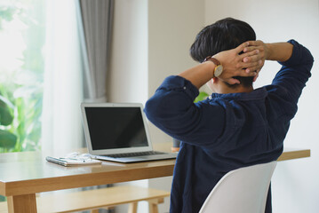 Young businessman wearing blue shirt sitting at your desk clasp your hands on the back of your head at home suffering from headache desperate and stressed because pain and migraine.