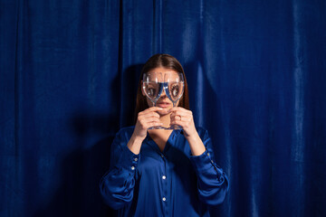 Woman over a blue background, holding a glass of water over her face 