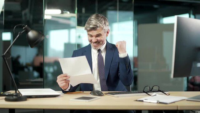 satisfied mature businessman in suit reads a document. happy Handsome young man looking and checking at paper letter correspondence with good results, smiling. entrepreneur joy from a signed contract