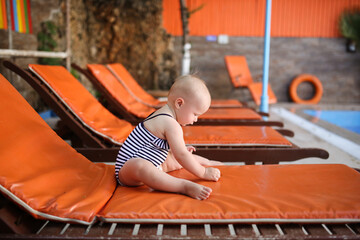 Cute baby toddler in swimsuit on wooden sun lounger orange, summer vacation with children