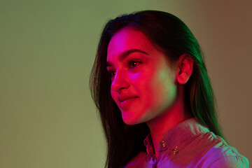 Fototapeta premium Half-length portrait of young pretty girl with long dark hair posing isolated on grey background in neon light. Concept of beauty, art, fashion, youth and emotions