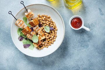 Halloumi and chicken kebabs served with roasted chickpeas in a beige plate, above view on a light-blue stone background with space