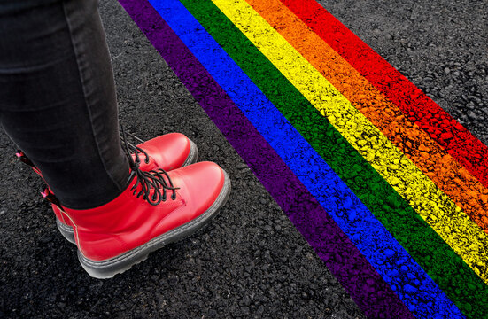 a woman with a boots is standing on asphalt next to Rainbow drawn LGBT pride flag

