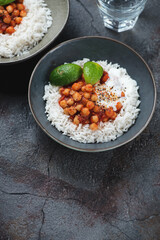 Chana masala or curried dish with chickpeas, onions, tomatoes, spices and herbs, vertical shot on a dark-grey asphalt background with copy space