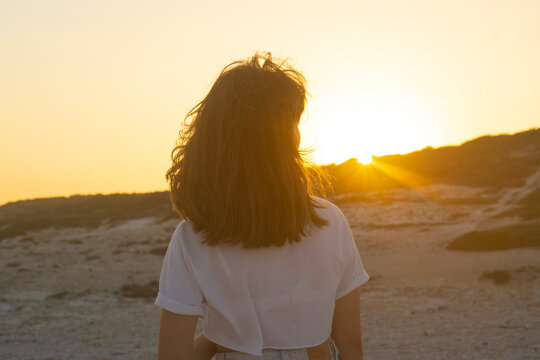 A teenage girl looks at the sunset on the beach. relaxed girl in the rays of the setting sun. Sad for a loved one alone