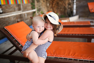 Cute baby toddler and sister kid girl in hat and sunglasses in swimsuit together on wooden sun...