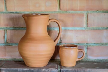 A clay jug and a mug against the background of the brick wall of an old fireplace in the countryside.