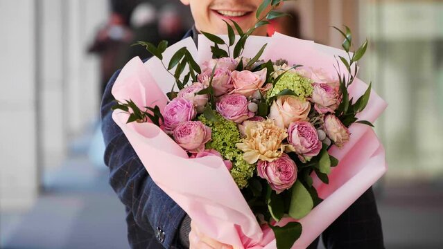Young man with bouquet of beautiful flowers outdoors, closeup. Slow motion effect