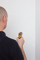 Save energy concept: man measuring the temperature of an external white wall with an infrared or...