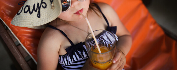 Cute child girl in wide-brimmed hat and sunglasses in swimsuit on wooden sun lounger orange, summer...