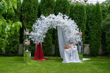 Wedding arch of white flowers and other elements of wedding design on the green lawn