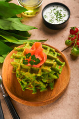 Green Belgian waffles. Spinach or wild garlic or pesto waffles with red salmon and cream sauce on old beige tile table background. Delicious breakfast, snack, brunch on old beige tiles background.
