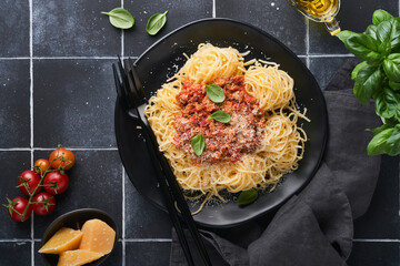 Tagliatelle pasta with meatballs in tomato sauce, basil and parmesan cheese on black stone or concrete background. Traditional Italian dish and cuisine. Top view with copy space.