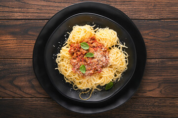 Pasta spaghetti Bolognese. Tasty appetizing italian spaghetti with bolognese sauce, tomato sauce, cheese parmesan and basil on white plate on old wooden rustic table background. Top view.