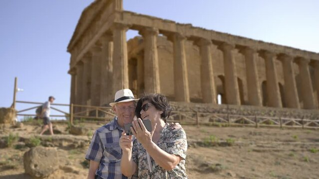 A cheerful mature couple takes a selfie in the Valley of the temples, in front of the Temple of Concordia, in Agrigento, an historical city of Sicily, in Italy.	