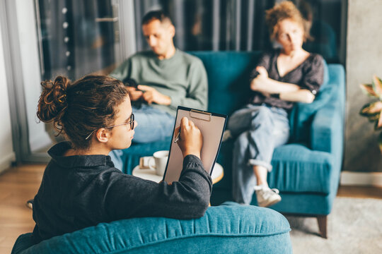 Middle Aged Family Couple Discusses Relationship Problems With Skilled Psychotherapist At Small Coffee Table In Light Clinic Office