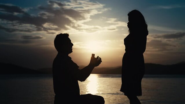 The guy makes a proposal to the girl to get married by the sea at sunset. Creating a new family and happy people together in a beautiful ocean landscape.