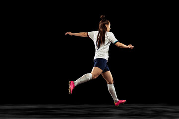 Fototapeta na wymiar Back view of energetic soccer, football player running isolated on dark background. Sport, action, competitions, games and fitness concept