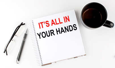 Coffee,glasses,pen and notebook written with IT'S ALL IN YOUR HANDS , on white background.