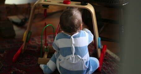 Candid baby playing indoors with toys. Infant sitting down on floor at playroom