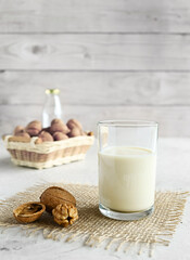 Vegan nut milk in a glass on a burlap and organic walnuts in a basket on a wooden table background, non-dairy alternative milk, copy space