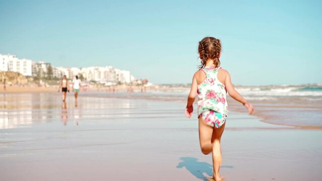 Child running ocean beach summer day Little girl caucasian have fun run on sand seashore Adorable female 5 years old enjoy playing on beach runs away from camera Handheld. High quality FullHD footage