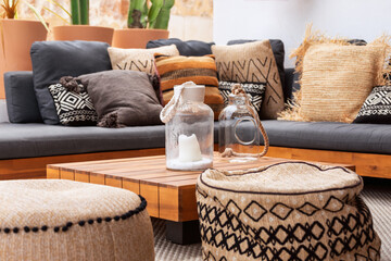 2 glass vases on a low wooden coffee table surrounded by two soft ottomans and a corner sofa with a...