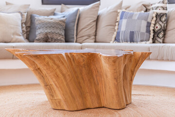 Coffee table made of a single solid natural wood surrounded by a sofa with countless cushions in the light living room of a Mediterranean villa