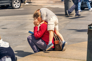 A child on a city street climbed on his mother's back to distract her from using a smartphone that...