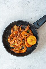 Grilled large shrimps (tiger) cooked in a frying pan with spices, herbs and lemon on a light background.