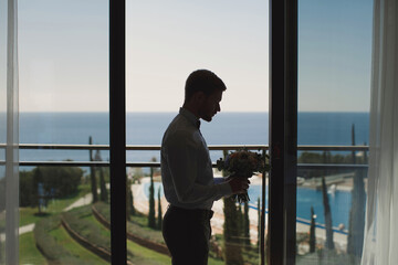 The silhouette of the groom with a bouquet on the background of the blue sea