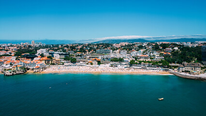 Fototapeta premium Drone aerial view of unidentifiable sunbathers at Praia da Conceicao beach in Cascais, Portugal