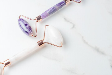 Pink Gua Sha massage tool on a white marble background, close-up. Rose Quartz and amethyst jade roller. Facial skin care at home, anti-aging and lifting therapy.