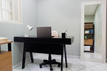 Home office with desk, laptop, lamp, mug and mirror. Modern classic interior design. Comfortable home office concept.
